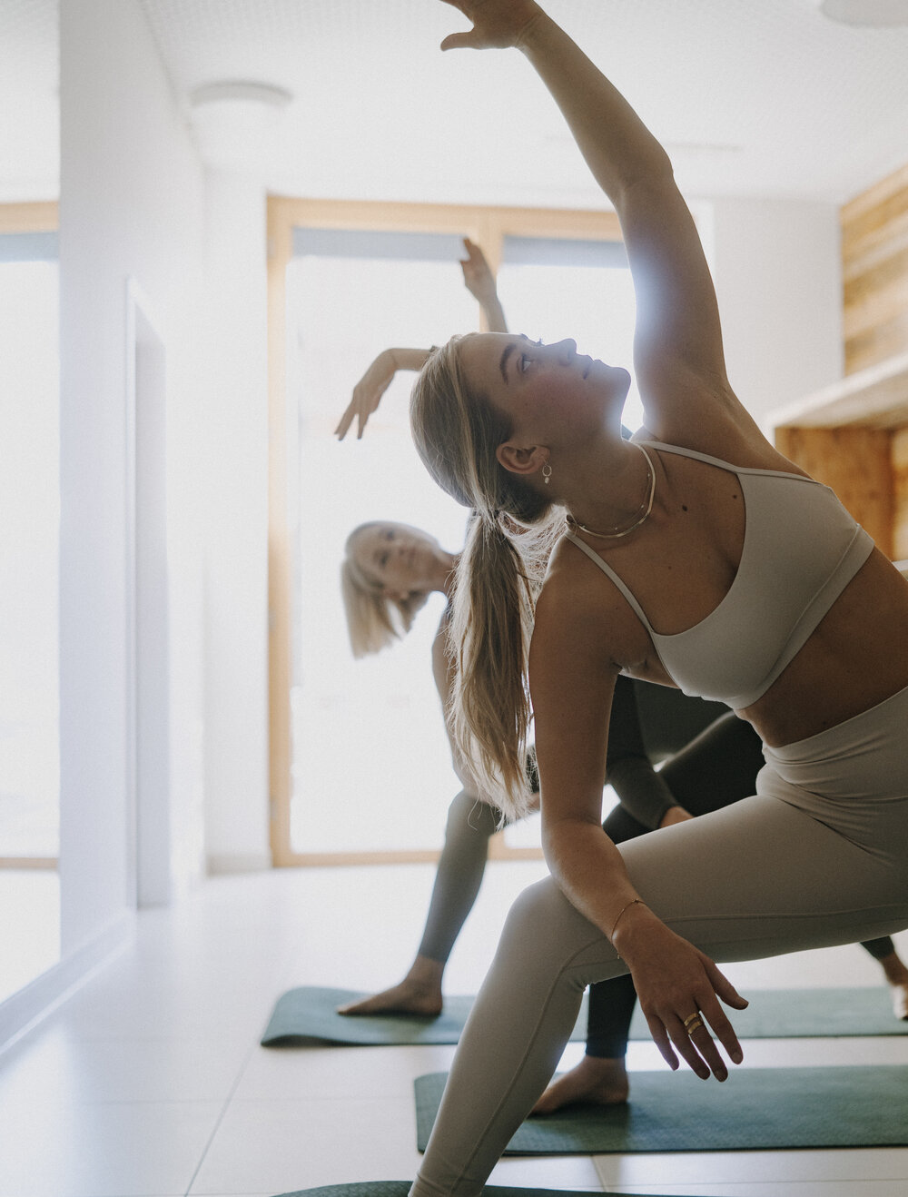 Woman in light athletic wear performing a yoga stretch with raised arm