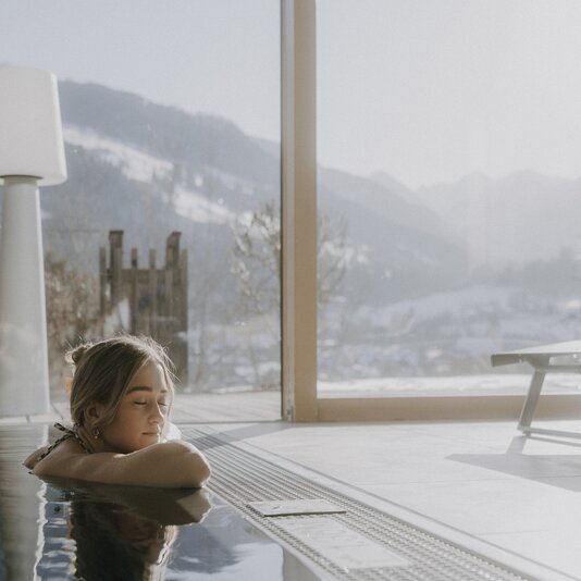 Person relaxing by indoor pool with mountain view