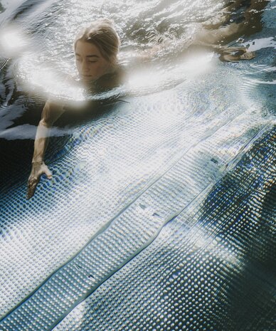 Person swimming underwater near pool edge with metal grid bottom