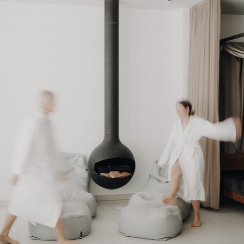Zwei Personen in weißen Bademänteln vor hängendem Kamin