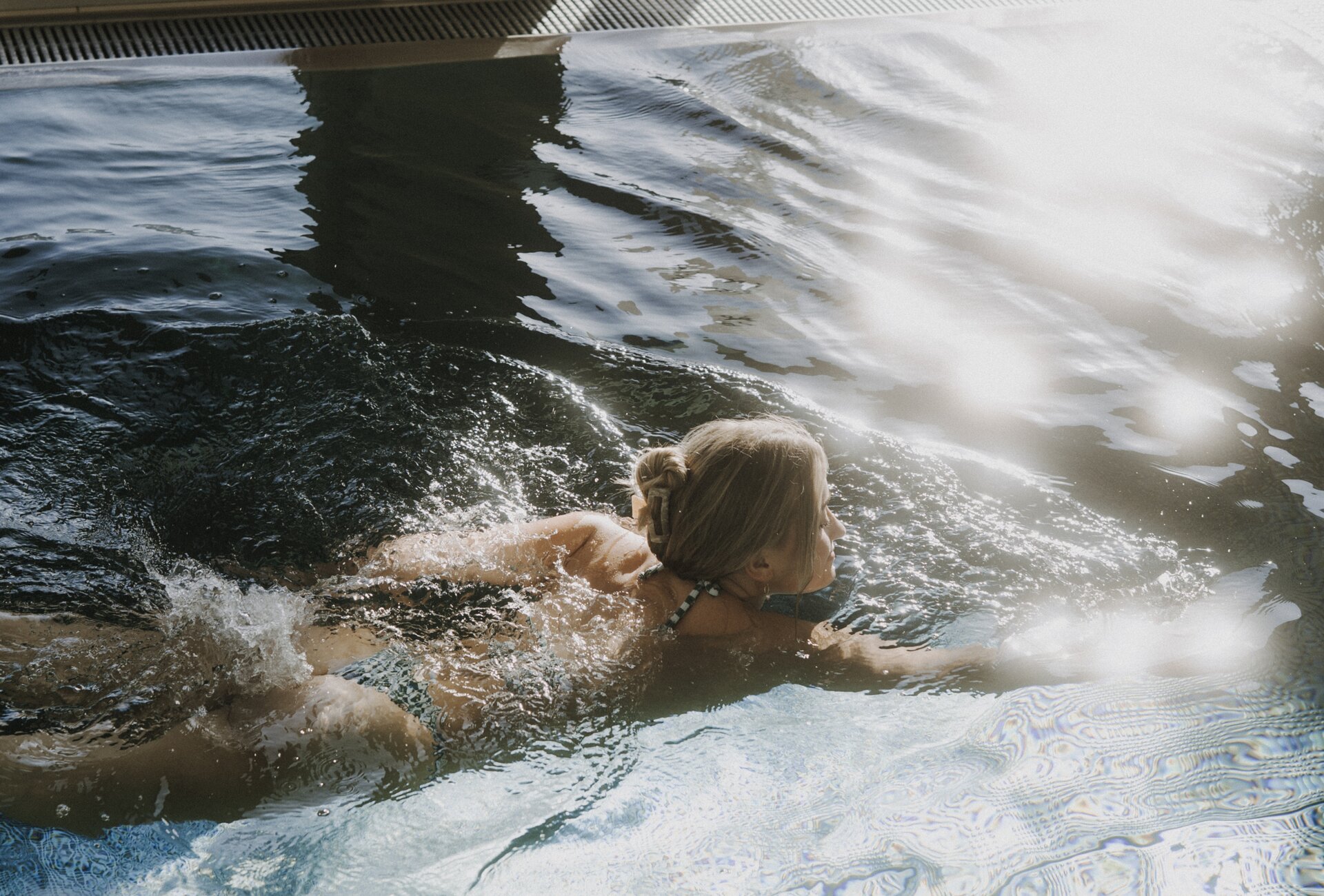 Person swimming in an indoor pool near glass doors.