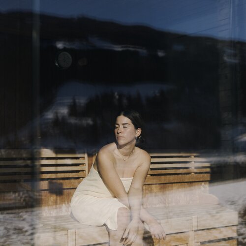 woman in towel sits with eyes closed inside glass-walled sauna