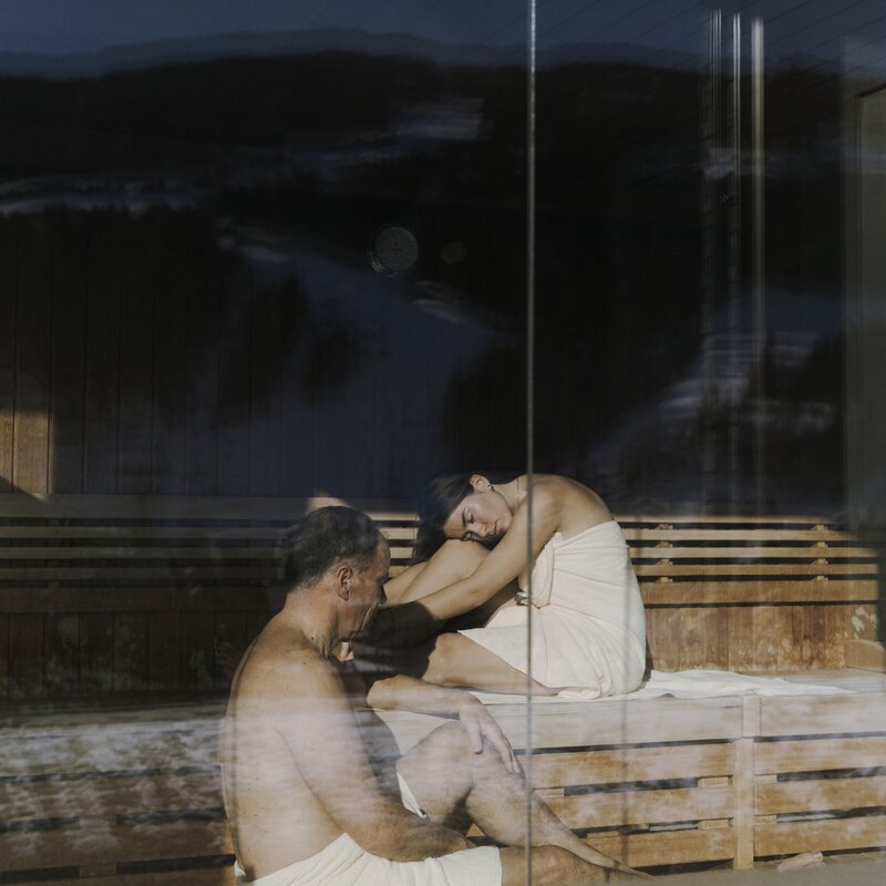 Two people in a wooden sauna, sitting on benches
