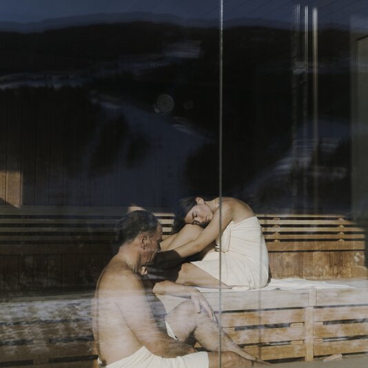 Two people in a wooden sauna, sitting on benches