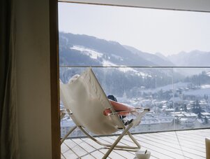 Person reclining in a woven lounge chair on balcony overlooking mountains