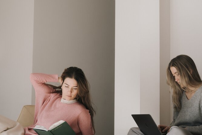 Two women in a modern living room; one reads, another works.