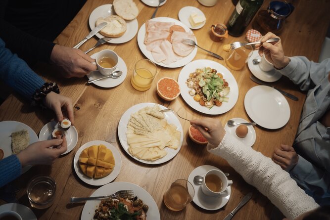 Group of people dining at a table with cheese, meats, bread.